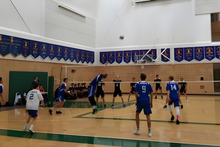Schüler der Reynolds Secondary School spielen Basketball auf einem Spielfeld mit Holzfußboden und weißen Wänden.