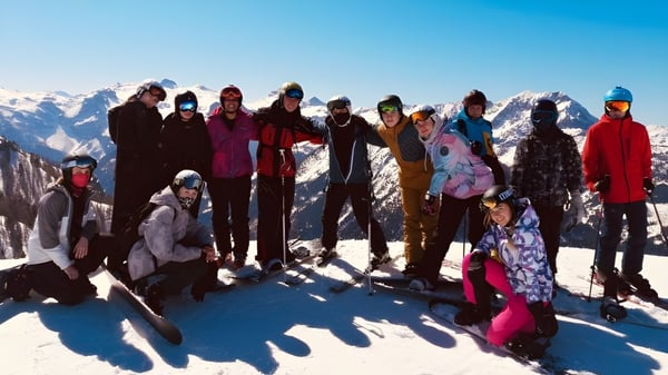 Eine Gruppe von Schülerinnen und Schülern der RGS Surrey Hills posiert in Winterkleidung auf einem verschneiten Hang mit Bergkulisse.