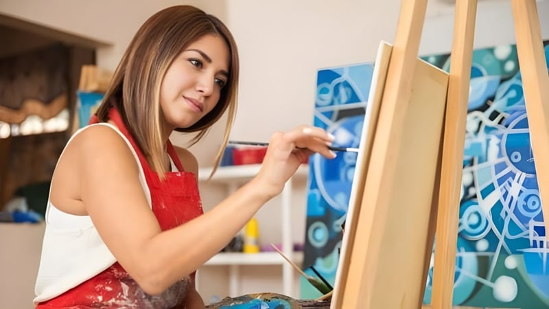 Eine Schülerin der Ribet Academy malt auf einer Leinwand in einem Atelier mit bunten abstrakten Bildern an den Wänden.