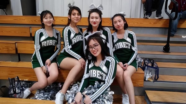 Eine Gruppe von Schülerinnen der Ribet Academy posiert gemeinsam in Sportuniformen vor einer Sporthalle.