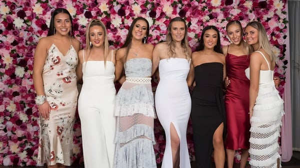 Sechs Schülerinnen in formeller Kleidung stehen vor einem bunten Blumenhintergrund auf dem Campus der Riccarton High School.