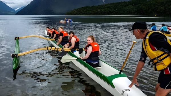 Schüler der Riccarton High School sitzen mit Rettungswesten in einem Boot auf einem See zwischen Bergen und Wäldern.