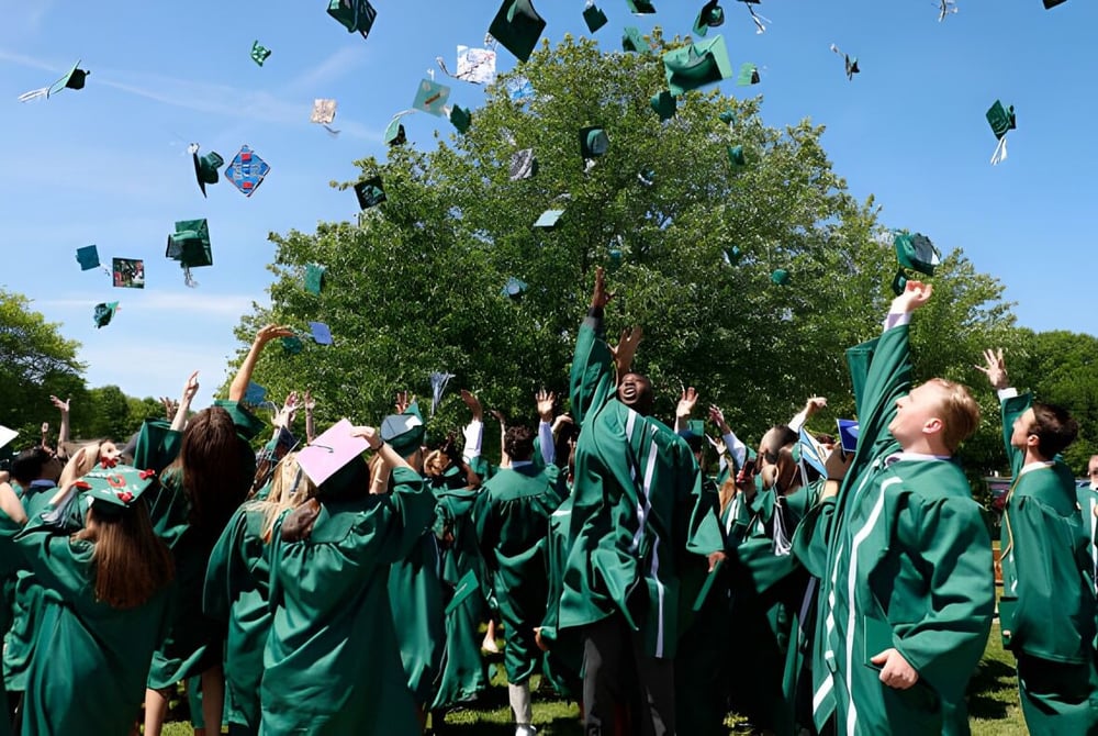Eine Gruppe von Absolventen der Rice Memorial High School wirft ihre grüne Abschlussmützen unter einem Baum in den blauen Himmel.