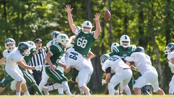 Eine Gruppe von Footballspielern der Rice Memorial High School spielt auf einem Spielfeld umgeben von Bäumen.