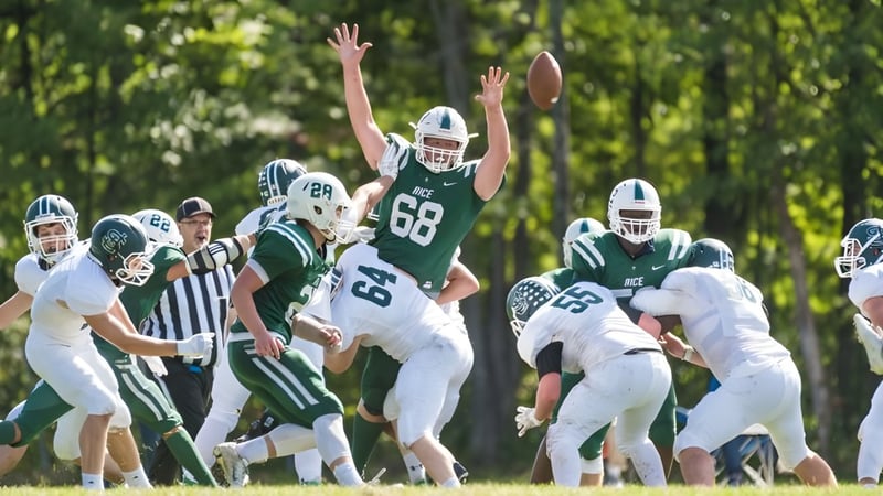 Eine Gruppe von Footballspielern der Rice Memorial High School spielt auf einem Spielfeld umgeben von Bäumen.