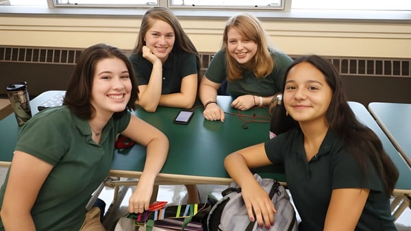 Vier Schülerinnen der Rice Memorial High School sitzen gemeinsam im Klassenraum und lächeln in die Kamera.