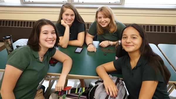 Vier Schülerinnen in grünen Uniformen sitzen zusammen und unterhalten sich auf dem Campus der Rice Memorial High School.