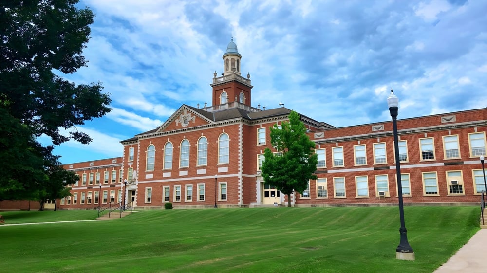 Das große Backsteingebäude mit hohem Turm auf dem grünen Rasen der Richmond High School unter einem bewölkten blauen Himmel.