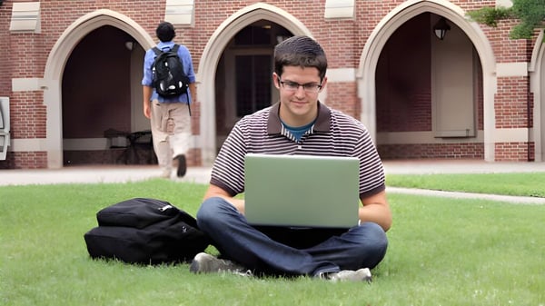 Ein Schüler der Richmond High School sitzt auf dem Rasen vor einem Backsteingebäude und arbeitet an einem Laptop.