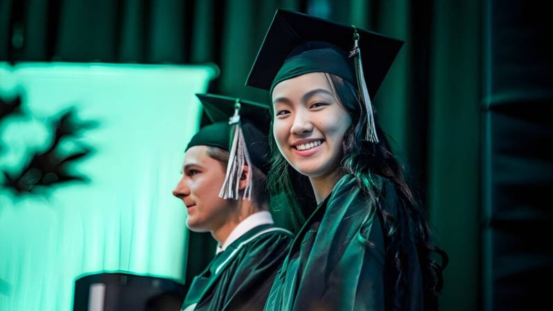 Zwei Absolventen in grünen Abschlussroben der Rick Hansen Secondary School stehen vor einem grünen Hintergrund.