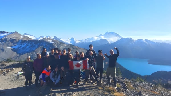 Eine Gruppe von Schülerinnen und Schülern der Rick Hansen Secondary School steht auf einem Bergrücken mit Blick auf schneebedeckte Gipfel und einen See.