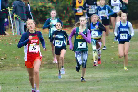 Schüler der Rick Hansen Secondary School nehmen an einem Crosslauf auf einem grasbewachsenen Feld mit Bäumen teil.