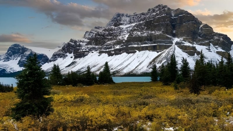 Ein schneebedeckter Berg erhebt sich über einem ruhigen See vor einer goldenen Wiese auf dem Gelände der Rideau District High School.