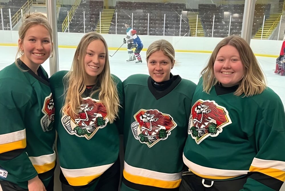 Vier Schülerinnen der Rideau District High School tragen grüne Hockeytrikots und stehen gemeinsam auf der Eisfläche der Eishockeyhalle.