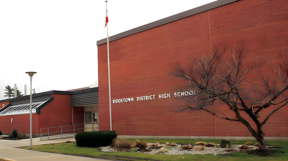 Das rote Backsteingebäude der Ridgetown District High School ist von einer gestalteten Außenanlage mit einem kahlen Baum umgeben.