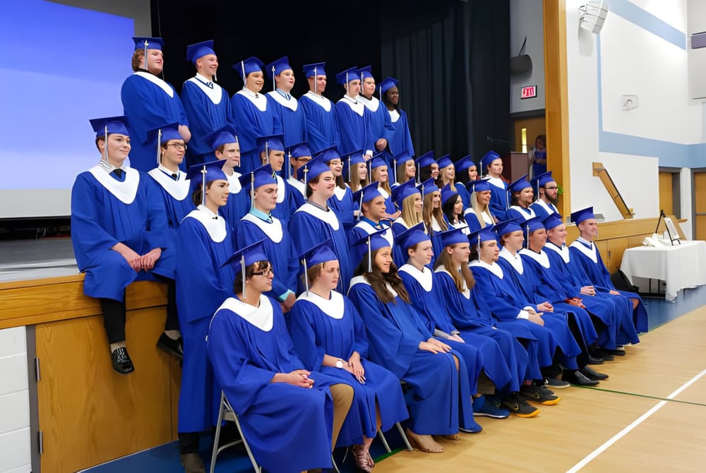 Eine große Gruppe von Absolventinnen und Absolventen der Ridgetown District High School steht auf der Bühne in blauen Talaren bei der Abschlussfeier.
