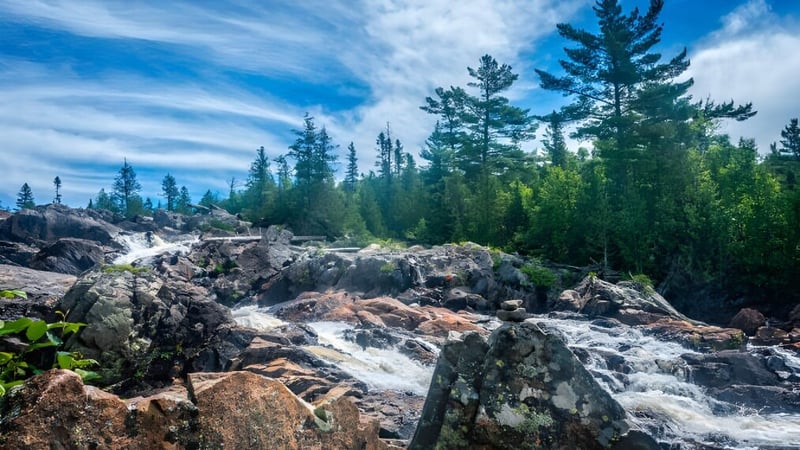 Eine felsige Landschaft mit Wasserfall und immergrünen Bäumen unter blauem Himmel in der Nähe der Ridgetown District High School.