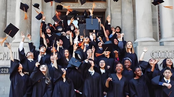 Eine große Gruppe von Absolventinnen und Absolventen in schwarzen Talaren und Hüten versammelt sich auf der Treppe eines historischen Gebäudes auf dem Campus von Ridley College.
