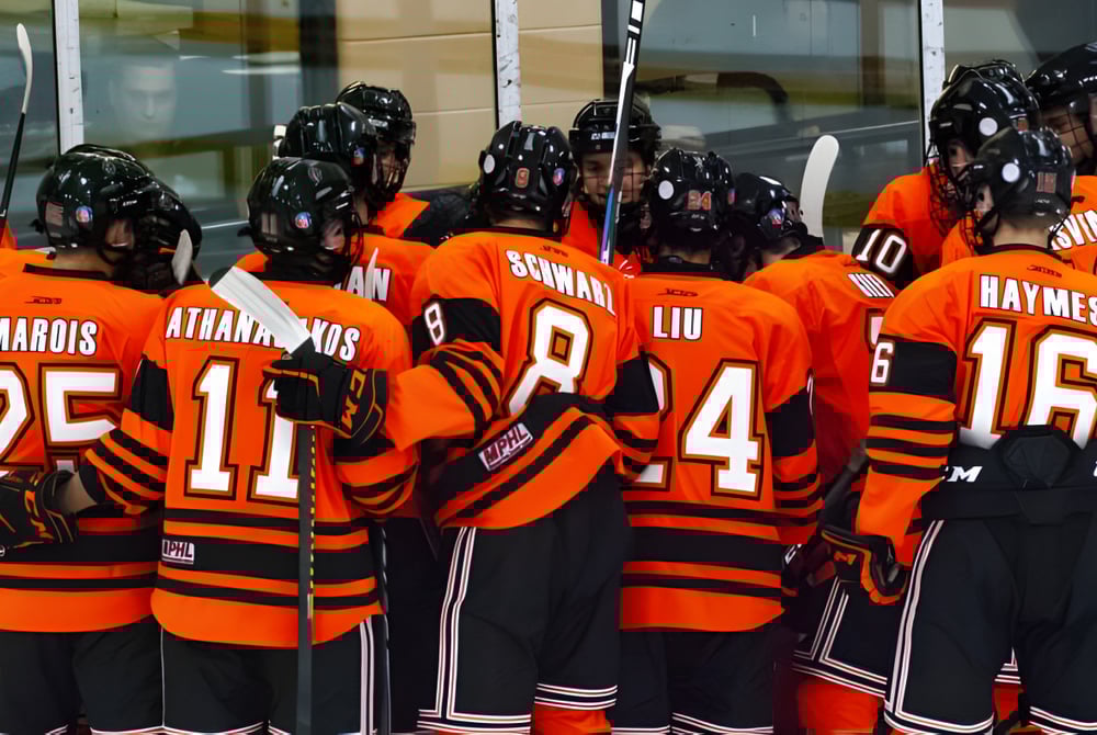 Eine Gruppe von Hockeyspielern in orangen Trikots steht gemeinsam vor einem Gebäude auf dem Campus des Ridley College.