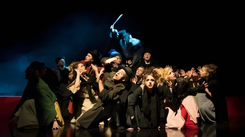 Eine Gruppe Schüler der Ringwood School steht in dunklen Kostümen auf einer Bühne mit dramatischer Beleuchtung.