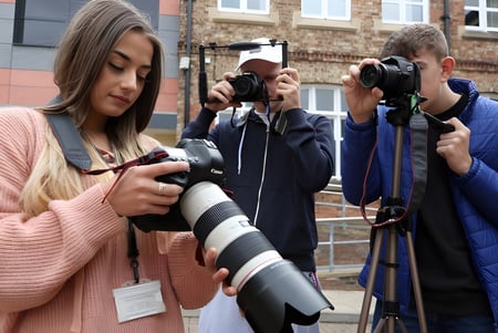 Eine Gruppe von Schülern der Ringwood School fotografiert mit Kameras vor Backsteingebäuden in der Stadt.