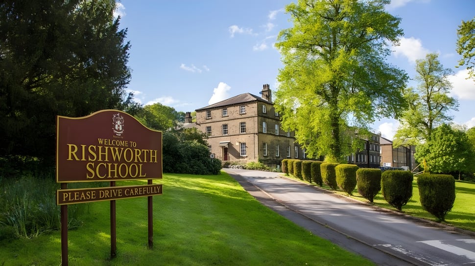 Das Willkommensschild der Rishworth School steht vor einem historischen Gebäude und umgeben von viel Grün.