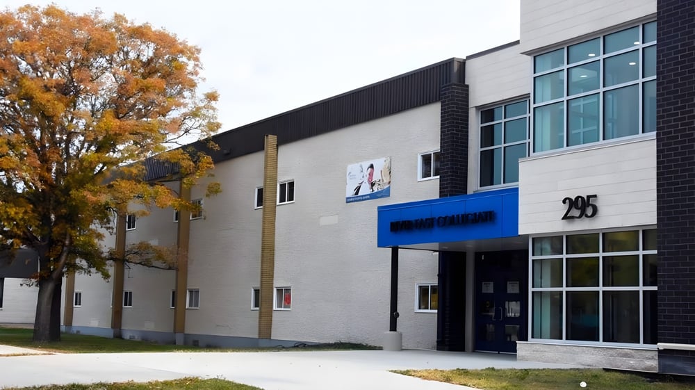 Das moderne mehrstöckige Gebäude des River East Collegiate ist umgeben von Bäumen mit herbstlichem Laub.