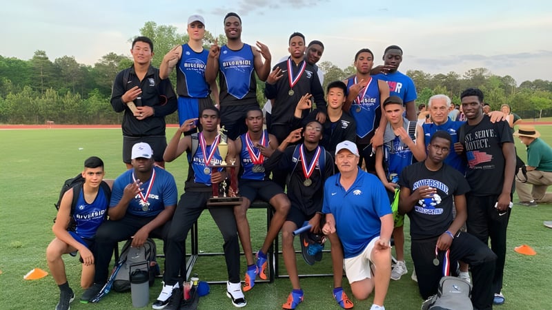 Eine Gruppe Schülerinnen und Schüler der Riverside Military Academy feiert auf dem Sportplatz mit Pokalen und Medaillen.