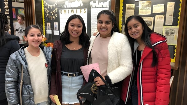 Vier Schülerinnen stehen gemeinsam im Flur der Riverside Secondary School vor mehreren Aushängen.