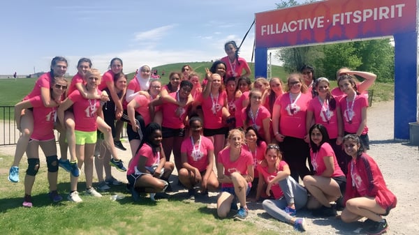 Eine Gruppe Schülerinnen der Riverside Secondary School posiert in einheitlichen pink-roten Uniformen vor dem Schriftzug Fillactive Fitspirit auf einem Feld.
