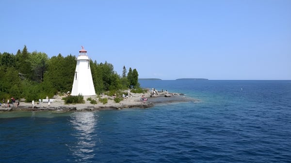 Ein malerischer Leuchtturm steht auf einem felsigen Vorsprung umgeben von Grün am Seeufer der Riverside Secondary School.