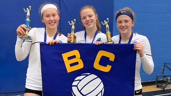 Drei Schülerinnen der Riverside Secondary School halten ein Banner mit den Buchstaben BC bei einem Sportereignis.