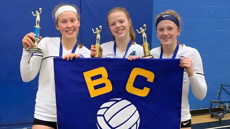 Drei Schülerinnen der Riverside Secondary School halten ein Banner mit den Buchstaben BC bei einem Sportereignis.