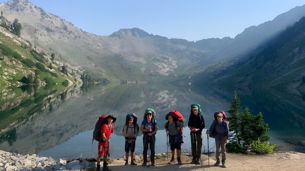 Eine Gruppe Schüler steht am felsigen Ufer eines Bergsees auf dem Gelände der Riverstone International School.