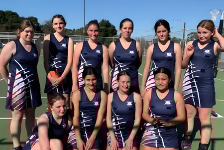 Eine Gruppe junger Athletinnen posiert auf dem Sportplatz der Riverton and District High School vor Bäumen und Gebäuden.