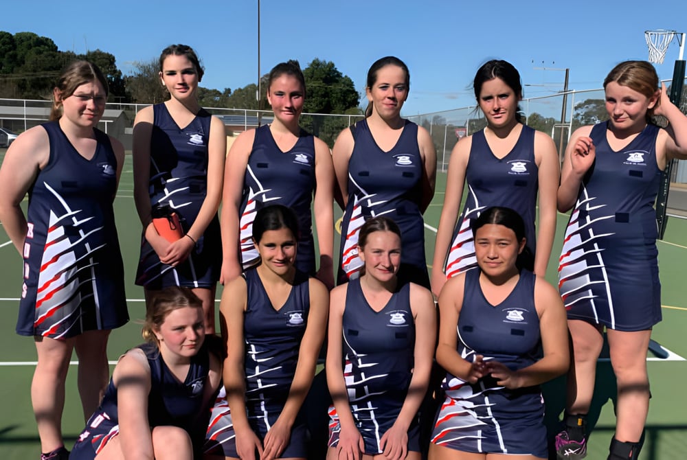 Eine Gruppe junger Athletinnen posiert auf dem Sportplatz der Riverton and District High School vor Bäumen und Gebäuden.