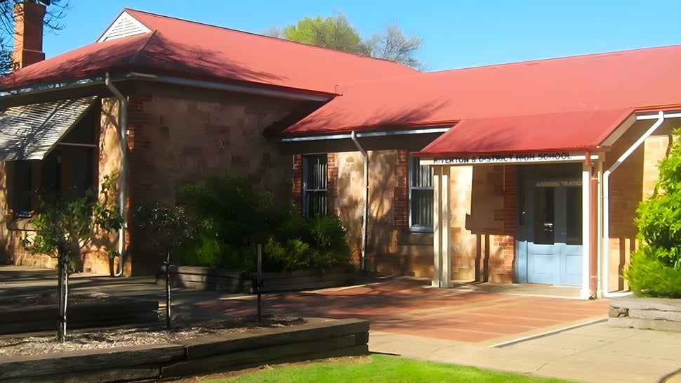 Das adobe-ähnliche Gebäude mit rotem Ziegeldach steht auf dem Campus der Riverton and District High School in grüner Umgebung.