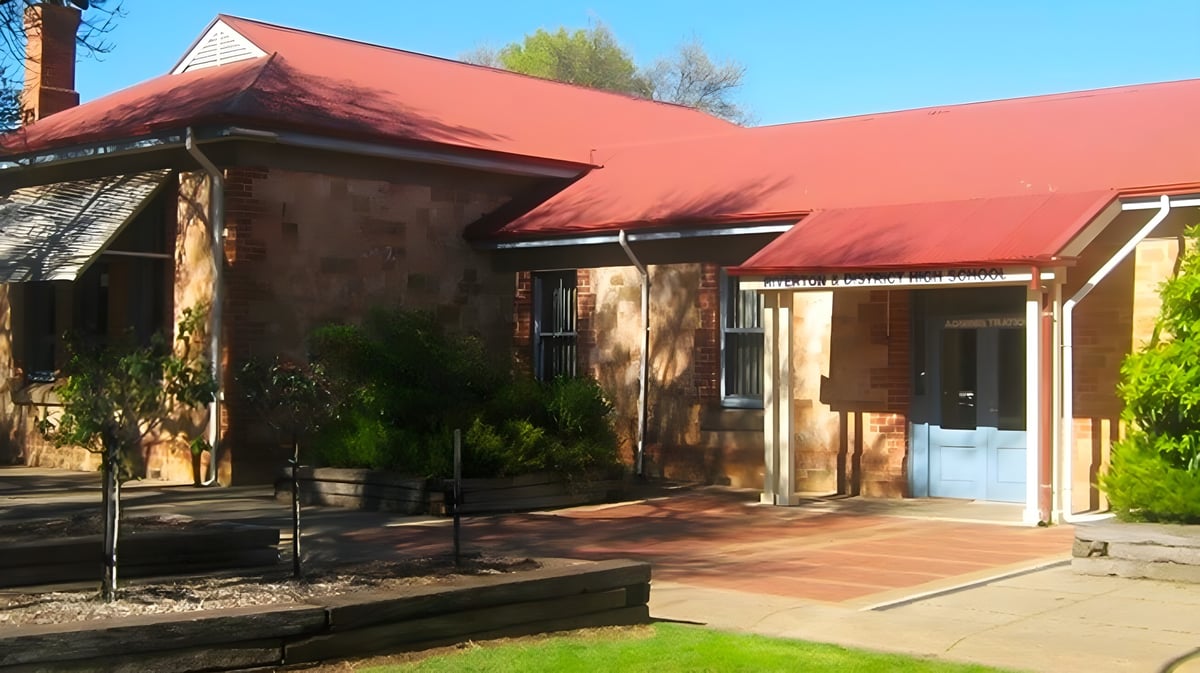 Das adobe-ähnliche Gebäude mit rotem Ziegeldach steht auf dem Campus der Riverton and District High School in grüner Umgebung.