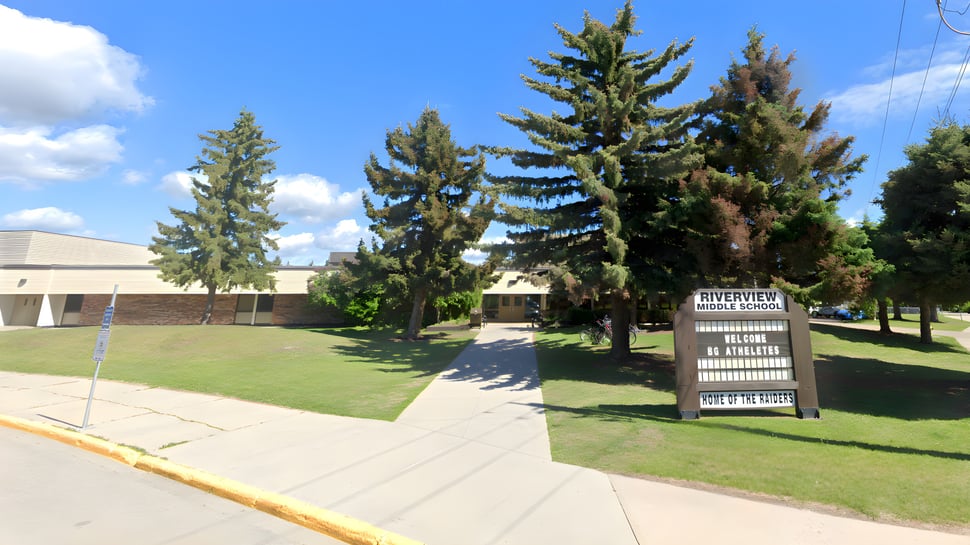 Eine Wiese mit hohen immergrünen Bäumen vor einem Gebäude auf dem Gelände der Riverview Middle School.