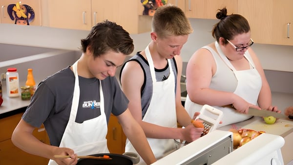 Schülerinnen und Schüler der Riverview Middle School arbeiten gemeinsam in einer Küche und bereiten Essen mit Küchengeräten zu.