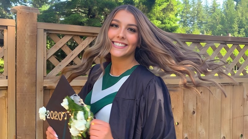 Eine Schülerin der Robert Bateman Secondary School steht lächelnd vor einem Holzzaun mit viel Grün im Hintergrund.