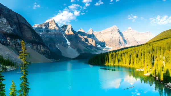 Ein ruhiger türkisfarbener See umgeben von schneebedeckten Bergen und grünen Wäldern nahe der Robert Thirsk High School.