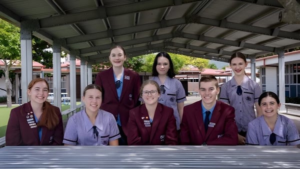 Eine Gruppe von Schülerinnen der Robina State High School steht in einheitlichen roten Uniformen unter einer überdachten Außenstruktur.