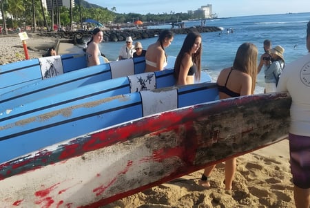 Eine Gruppe von Schülerinnen und Schülern der Robina State High School steht am Strand neben bunten Surfbrettern mit Stadtblick im Hintergrund.