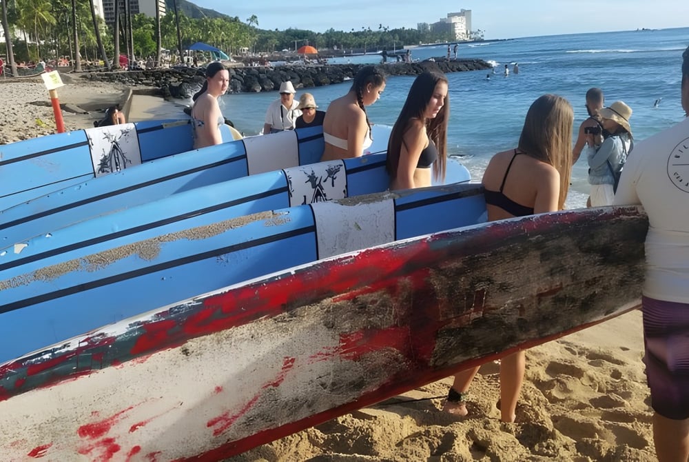Eine Gruppe von Schülerinnen und Schülern der Robina State High School steht am Strand neben bunten Surfbrettern mit Stadtblick im Hintergrund.