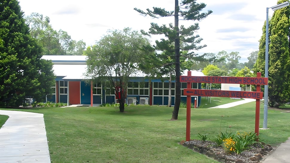 Der Campus der Rochedale State High School zeigt ein rotes Backsteingebäude, umgeben von Bäumen und einem Weg.