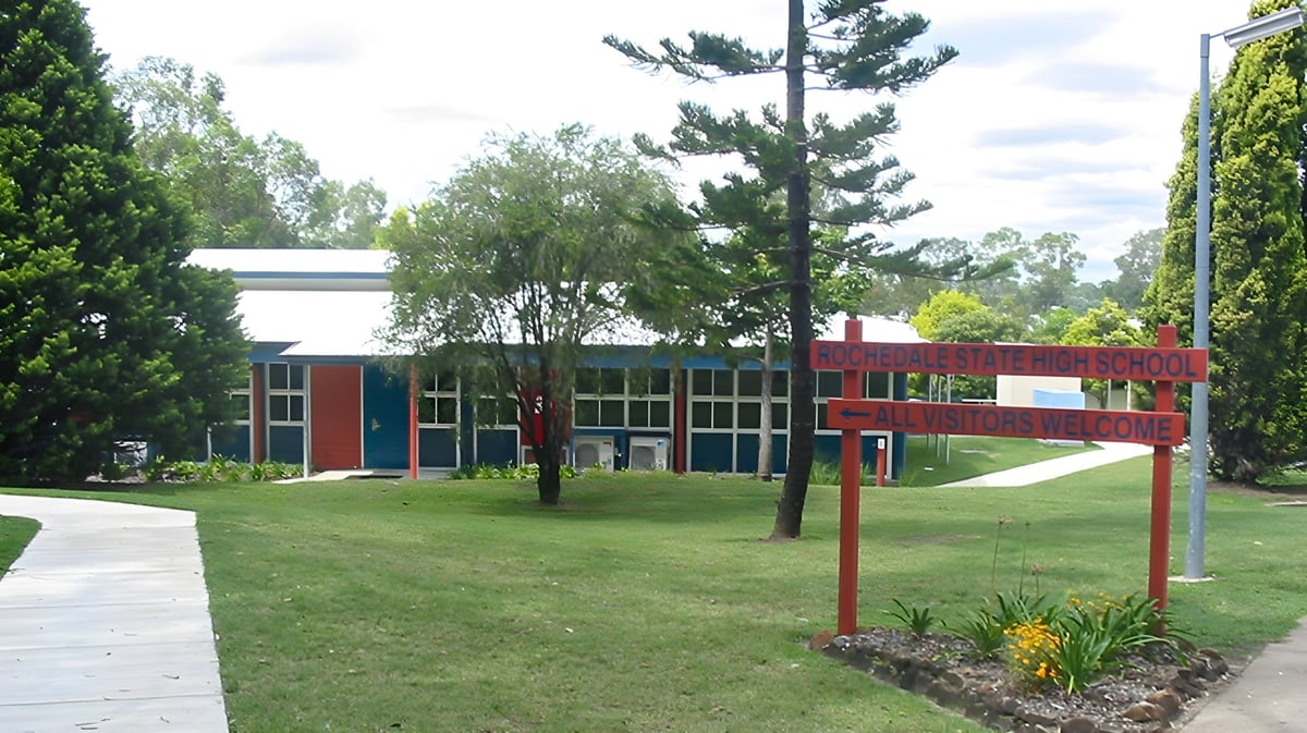 Der Campus der Rochedale State High School zeigt ein rotes Backsteingebäude, umgeben von Bäumen und einem Weg.