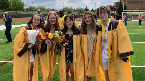 Eine Gruppe junger Frauen in Abschlusskleidung hält Blumen auf dem Sportfeld der Rochester Community Schools.