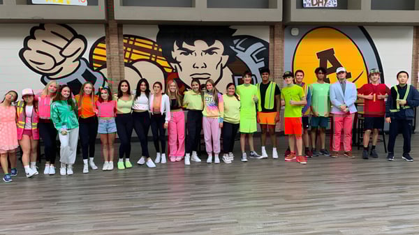 Eine Gruppe Schülerinnen und Schüler steht vor einer Wand mit farbenfroher Graffiti-Kunst auf dem Campus der Rochester Community Schools.