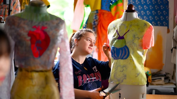 Eine Schülerin des Rochester Independent College steht aufmerksam zwischen bunten Kleidungsstücken in einem Textilraum.